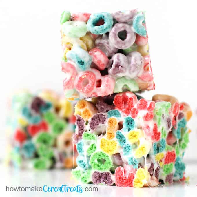 three Fruit Loops Cereal Treats are piled up on a white counter-top set in front of a white background