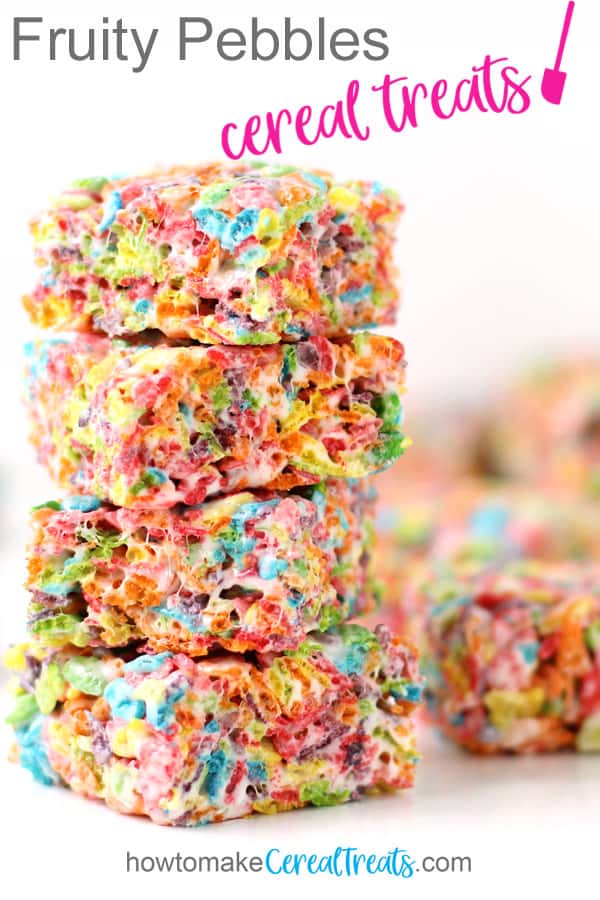 Four Fruity Pebbles Rice Crispy Treats are stacked up on the table set in front of a few more of the cereal treats on a white background.