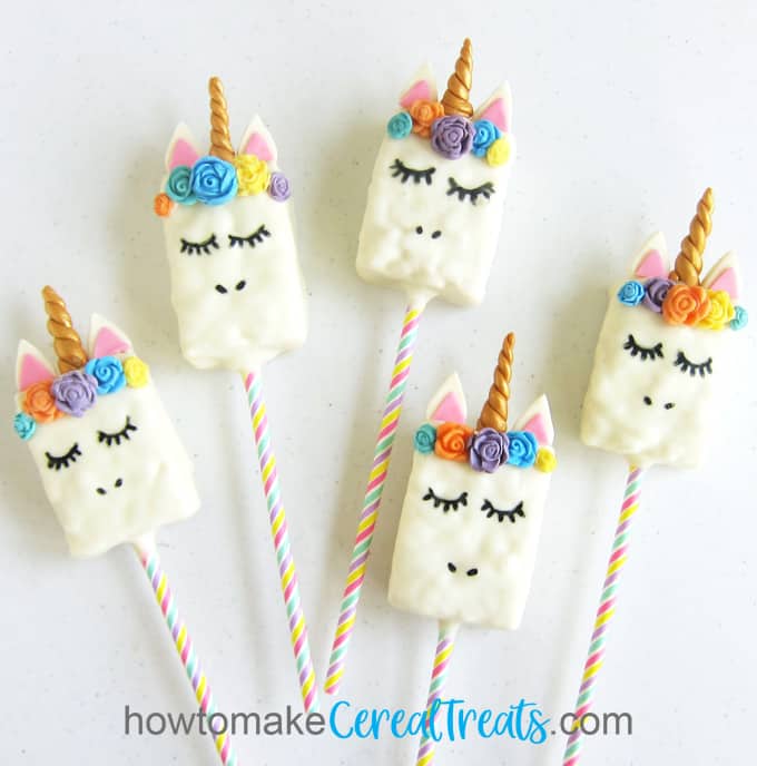 five Unicorn Rice Krispie Treats decorated with brightly colored modeling chocolate flowers, a gold horn and pink & white ears