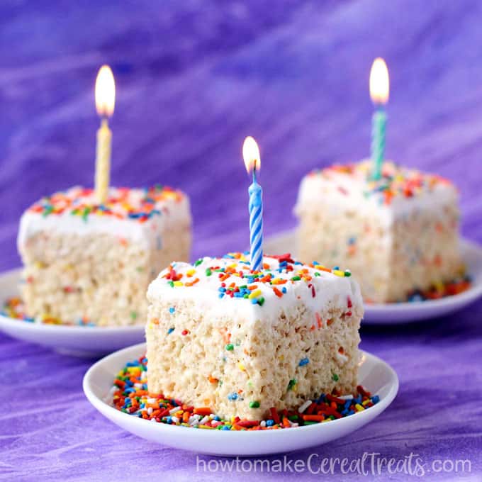 square birthday cake rice krispie treats served on white dessert plates with lots of rainbow sprinkles