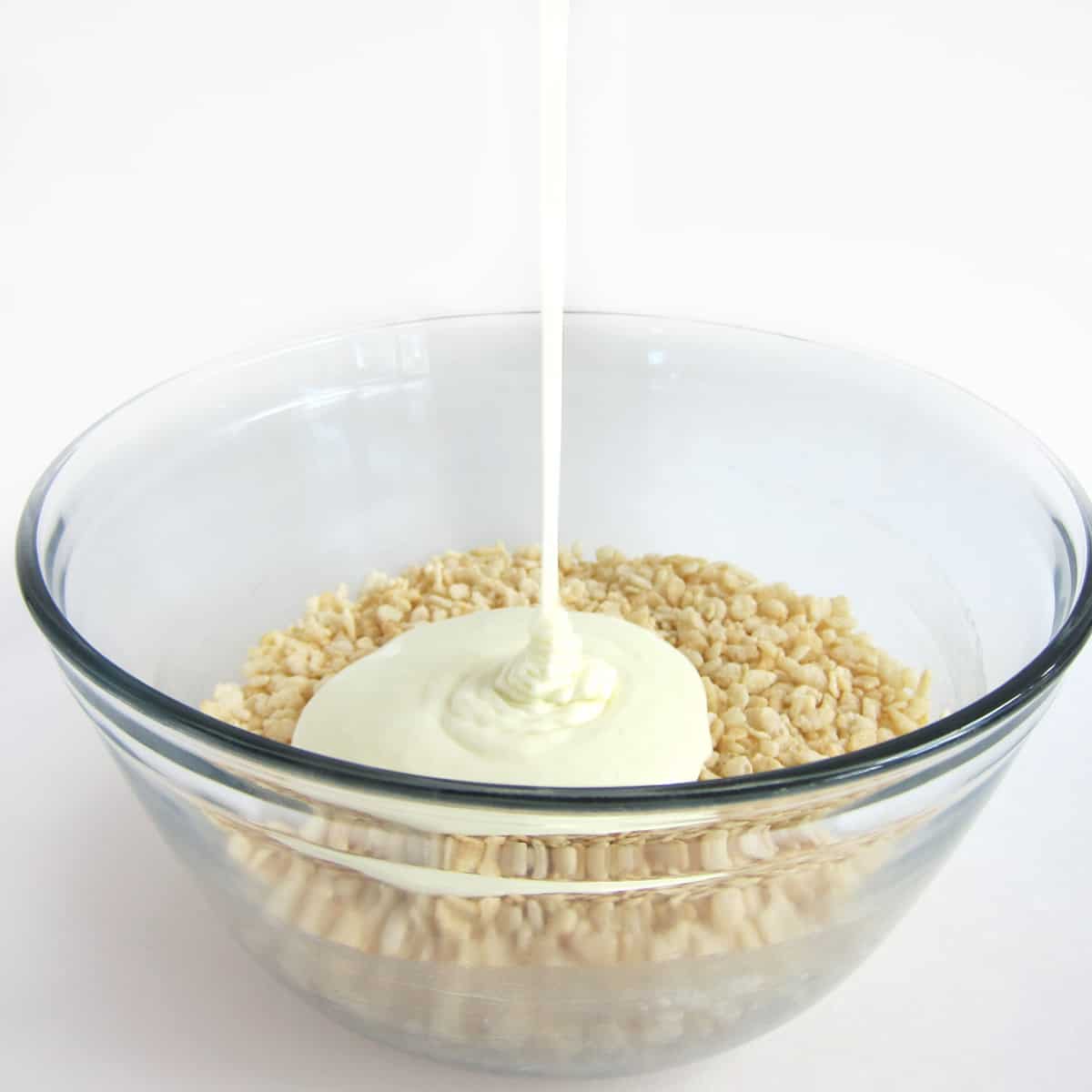 Pouring melted butter and marshmallows into a bowl of Rice Krispies cereal to make crispy treats.
