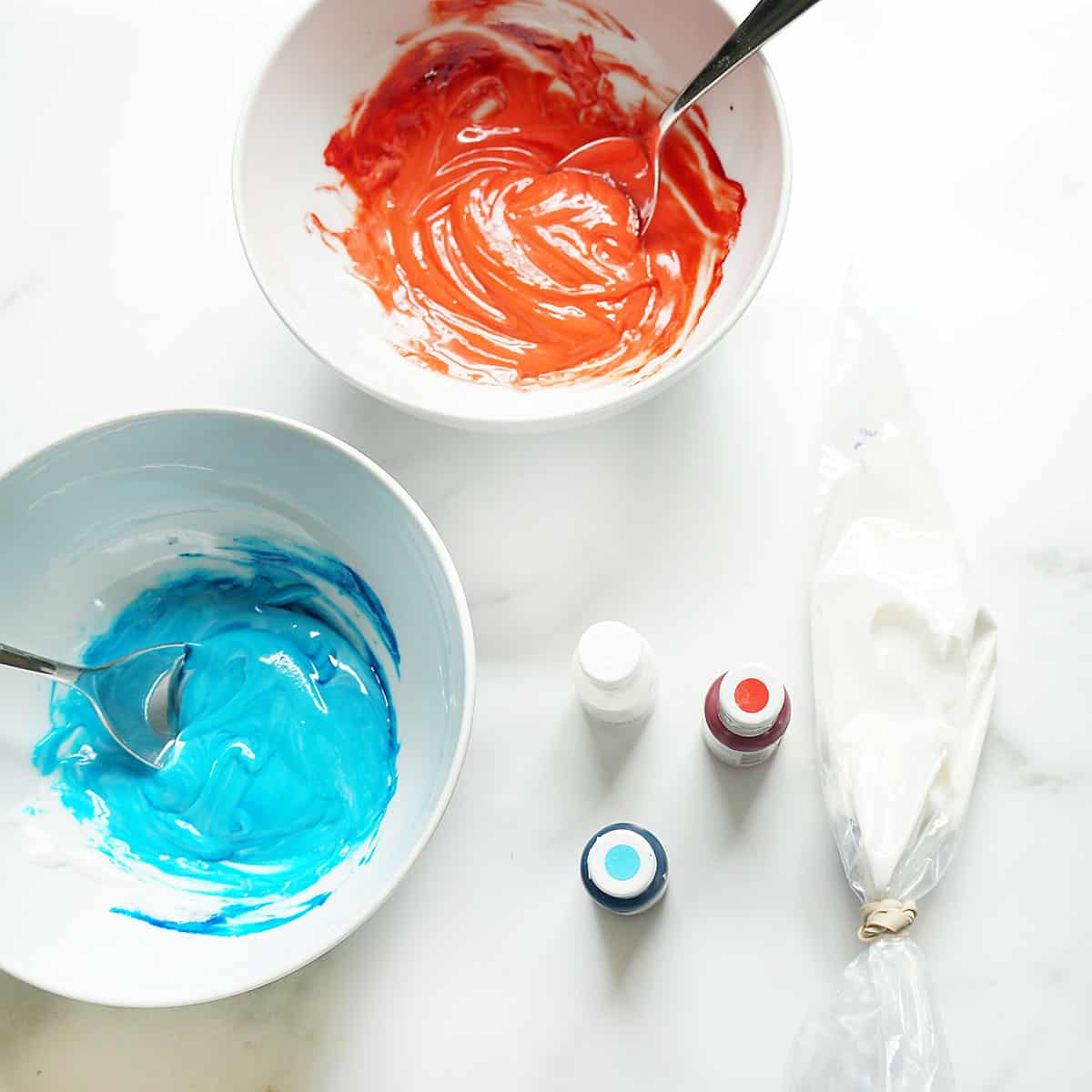 red, white, and blue icing in bowls with food coloring