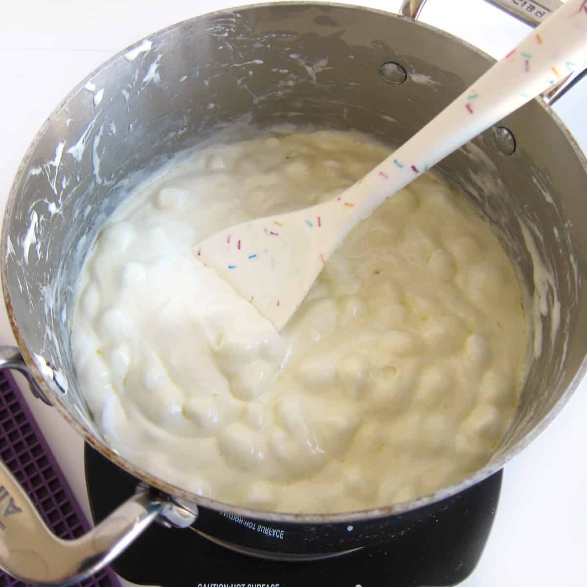 partially melted marshmallows in saucepan with silicone spatula