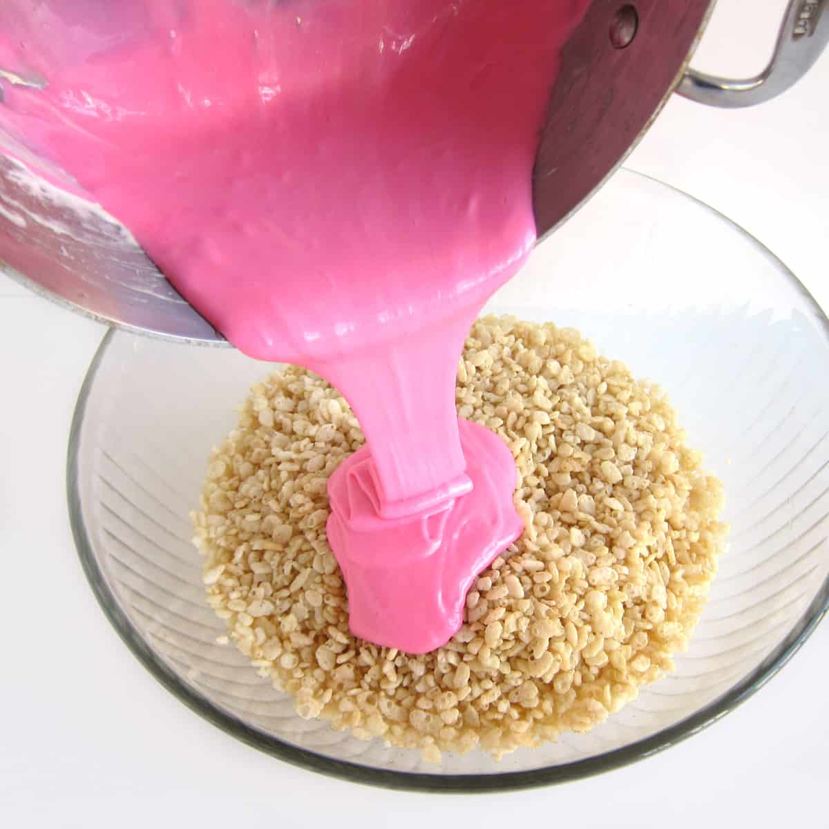 pouring bright pink melted marshmallows over a bowl of crisp rice cereal