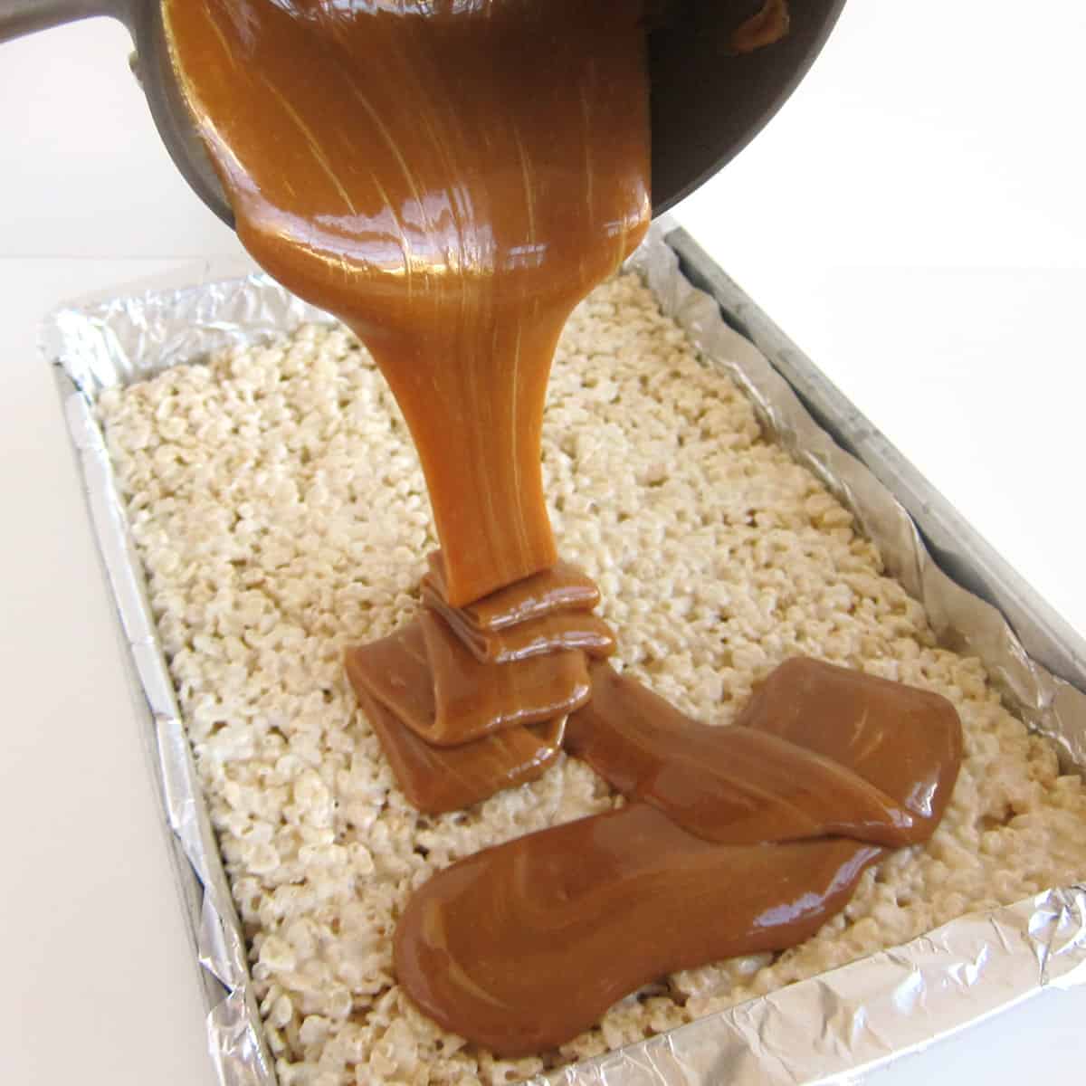 puring melted caramel over a pan of rice krispie treats