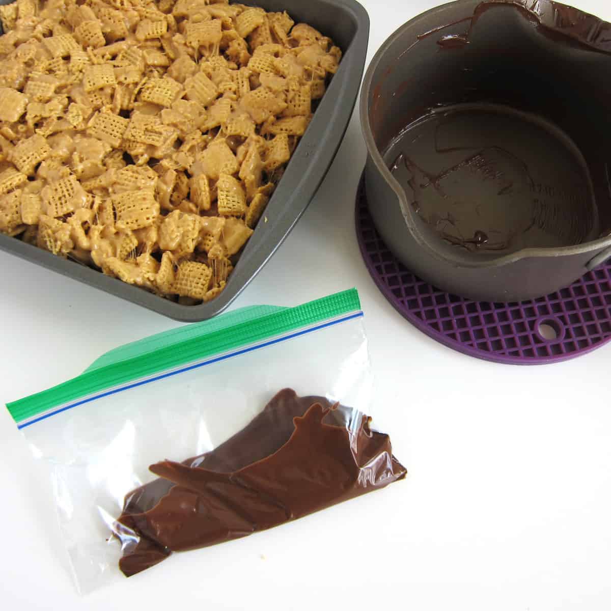 Chex Bars in pan next to an empty saucepan and a zip-top bag filled with melted chocolate and peanut butter