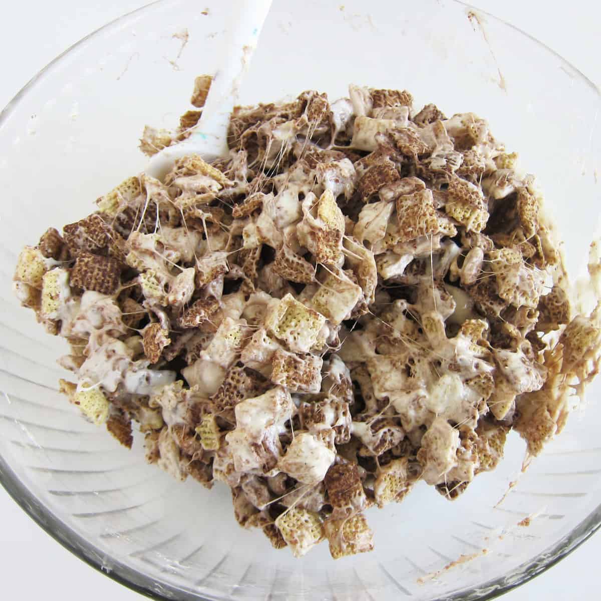 Stirring melted marshmallows and butter into Chocolate Chex cereal.