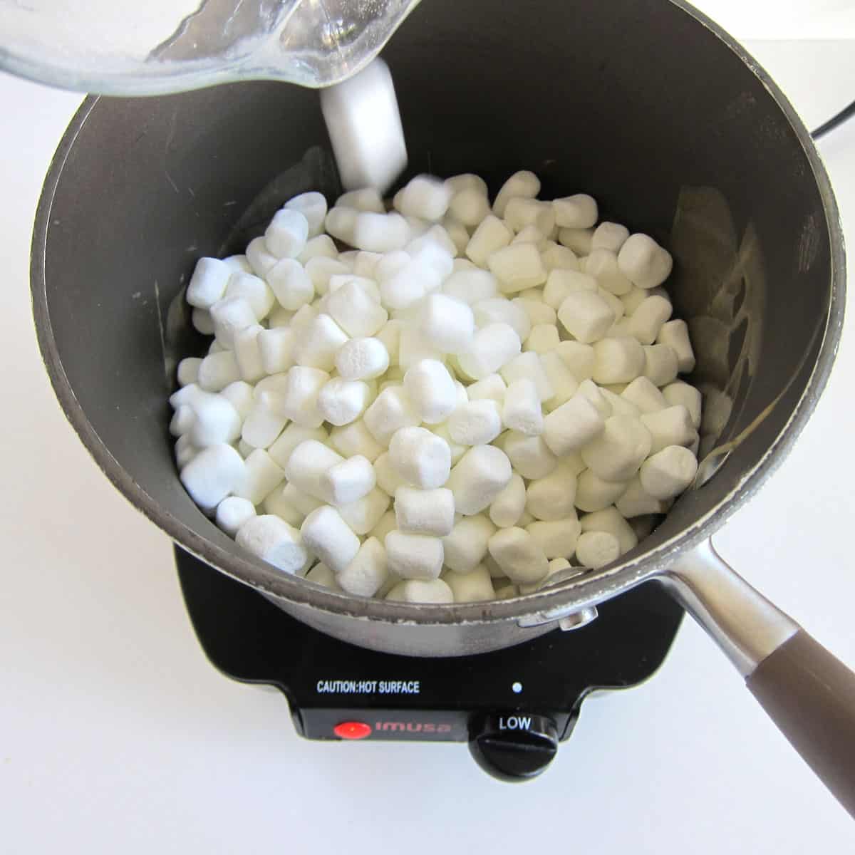 Pouring marshmallows into pan filled with melted butter and peanut butter.