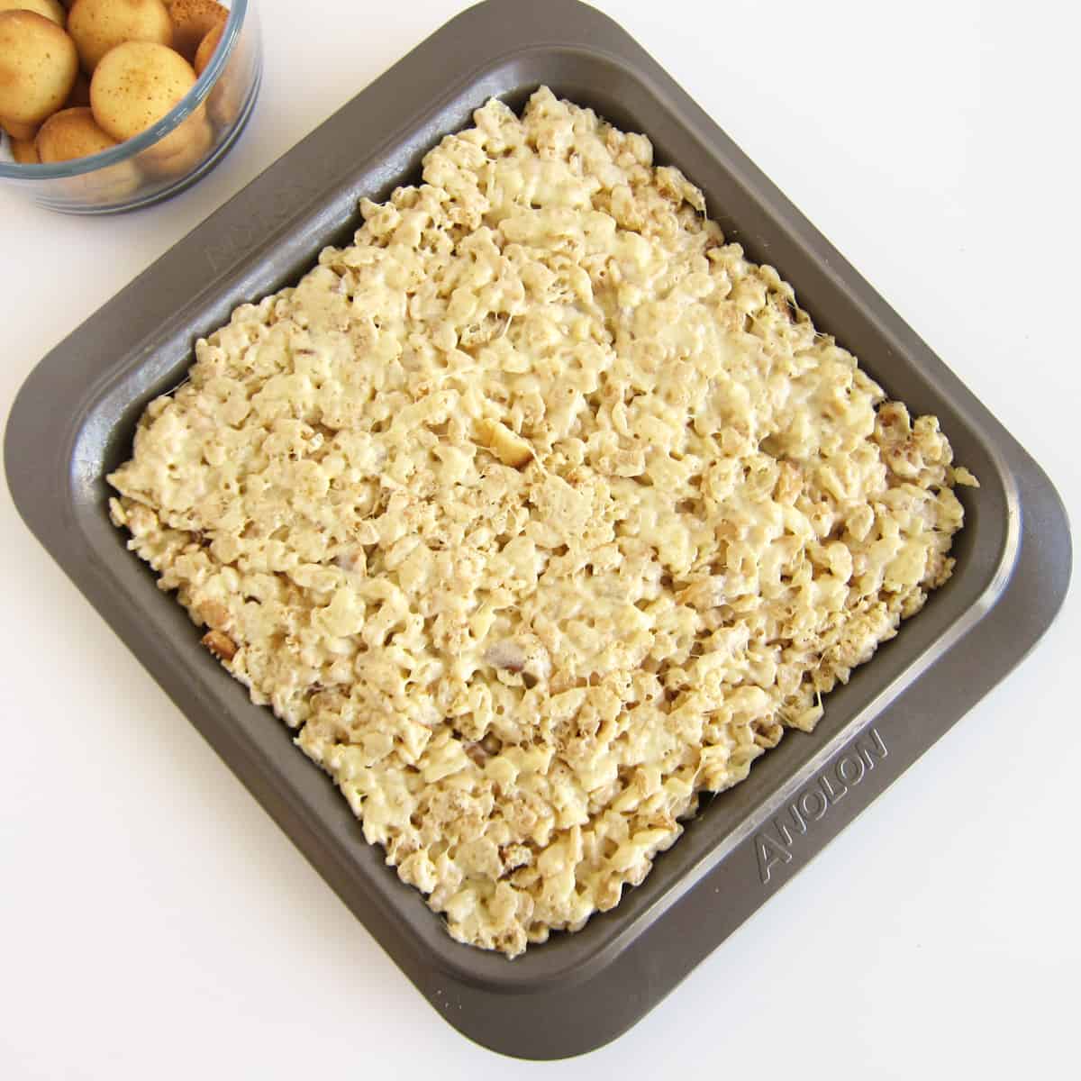 banana pudding rice krispie treats in a square 9-inch pan next to vanilla wafer cookies