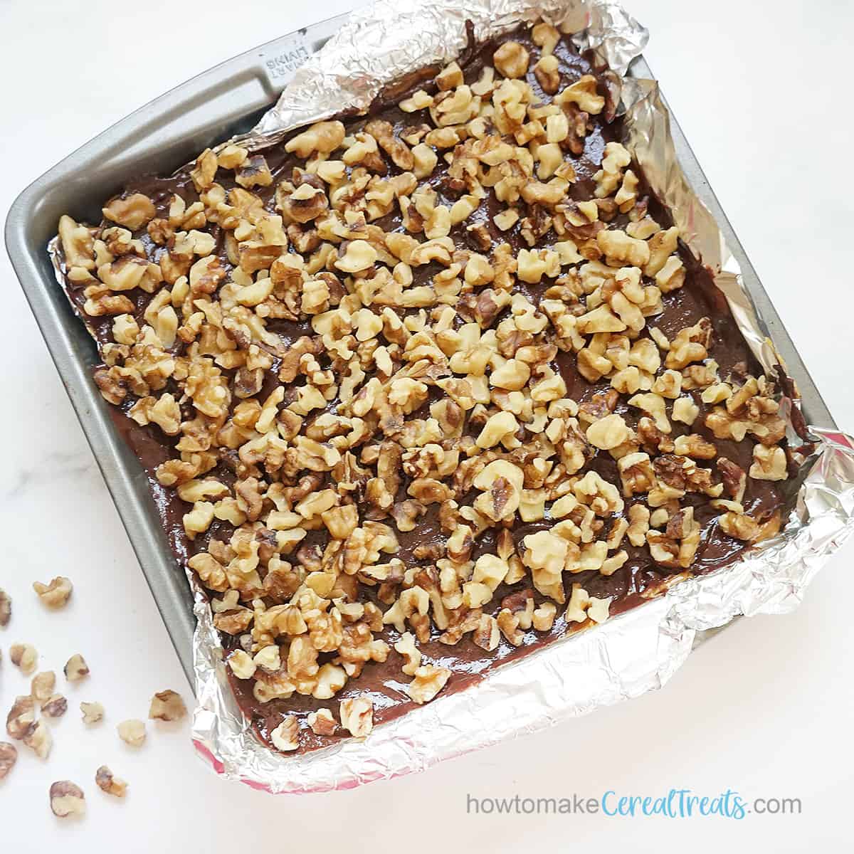 topping turtle rice krispie treats in baking pan with walnuts