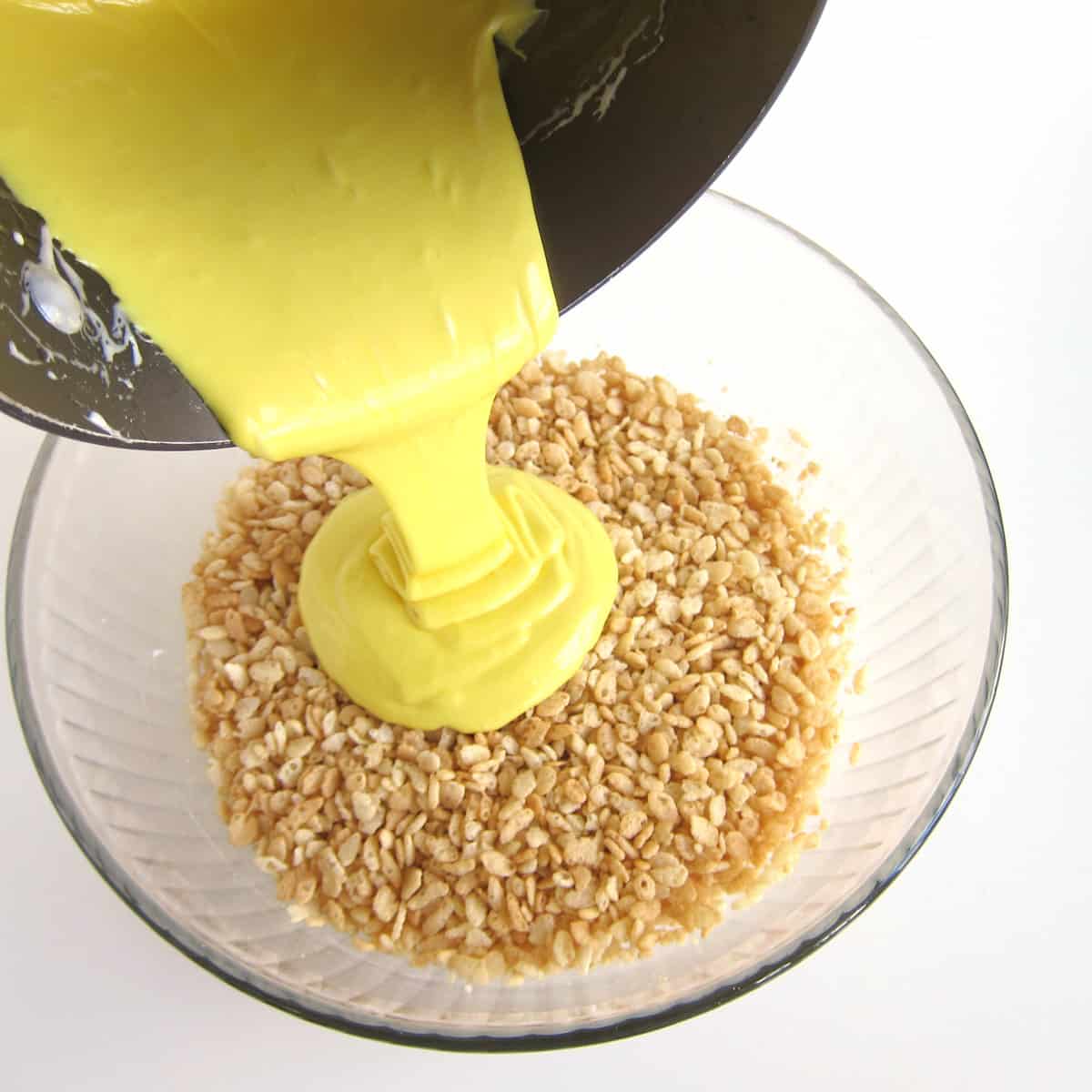 pouring yellow-colored melted marshmallows over a bowl of Rice Krispies cereal