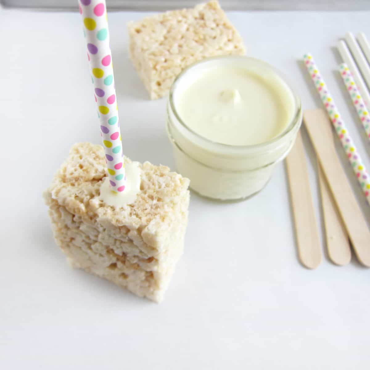 Rice Krispie treat with a polka dot paper straw inserted in one end secured with melted white chocolate.
