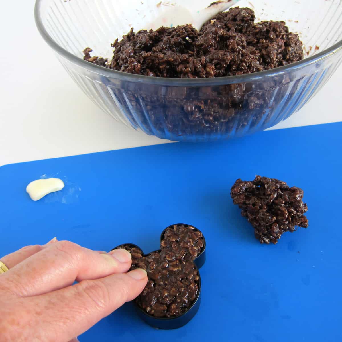 pressing chocolate rice krispie treat mixture into a Mickey Mouse cookie cutter
