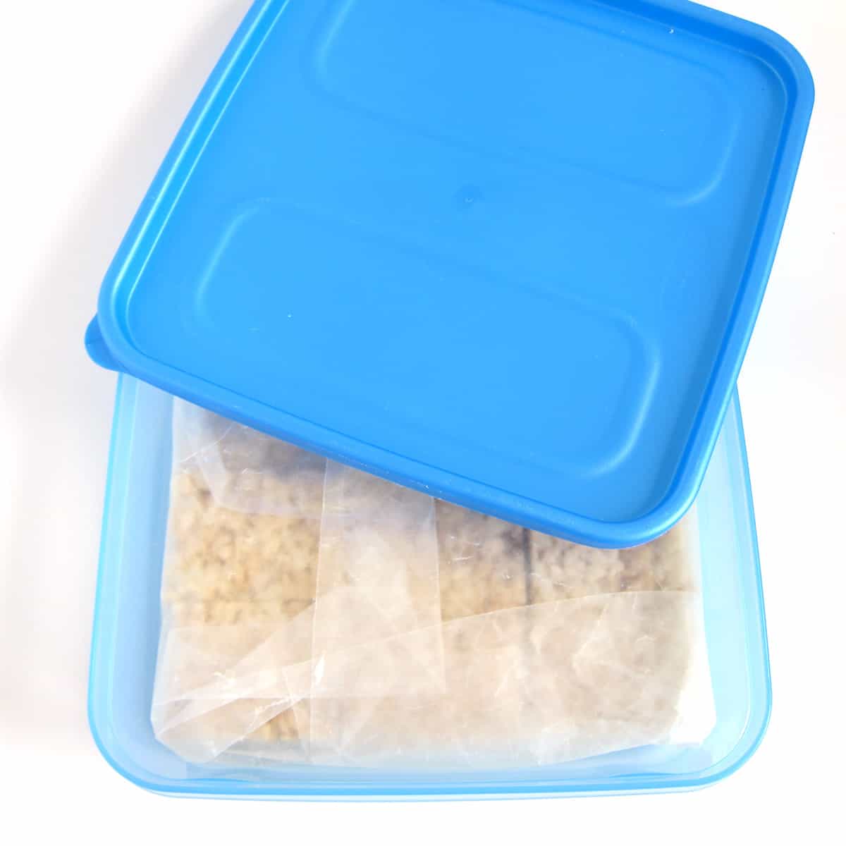 Rice Krispie Treats wrapped in wax paper in a freezer container.
