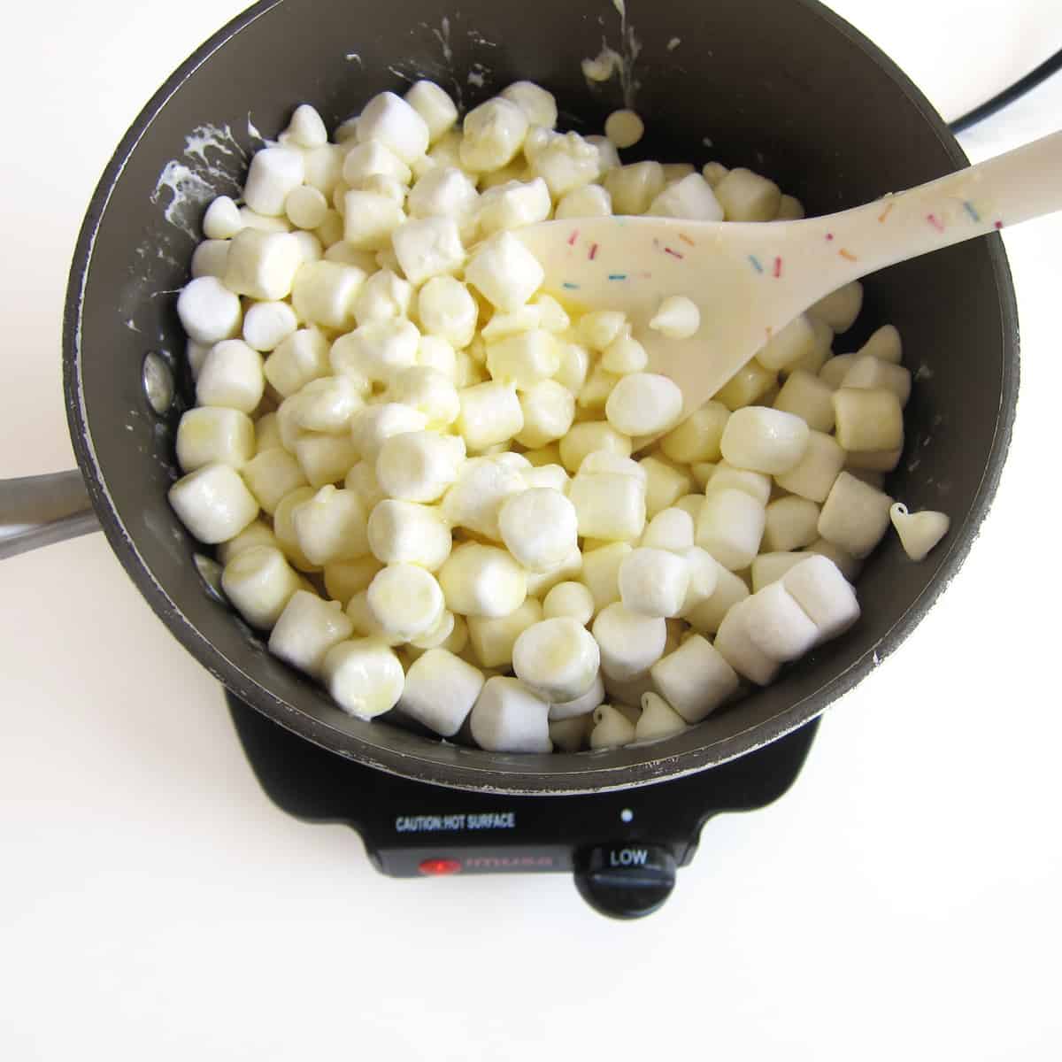 Stirring the melted butter with the mini marshmallows and white chocolate chips.
