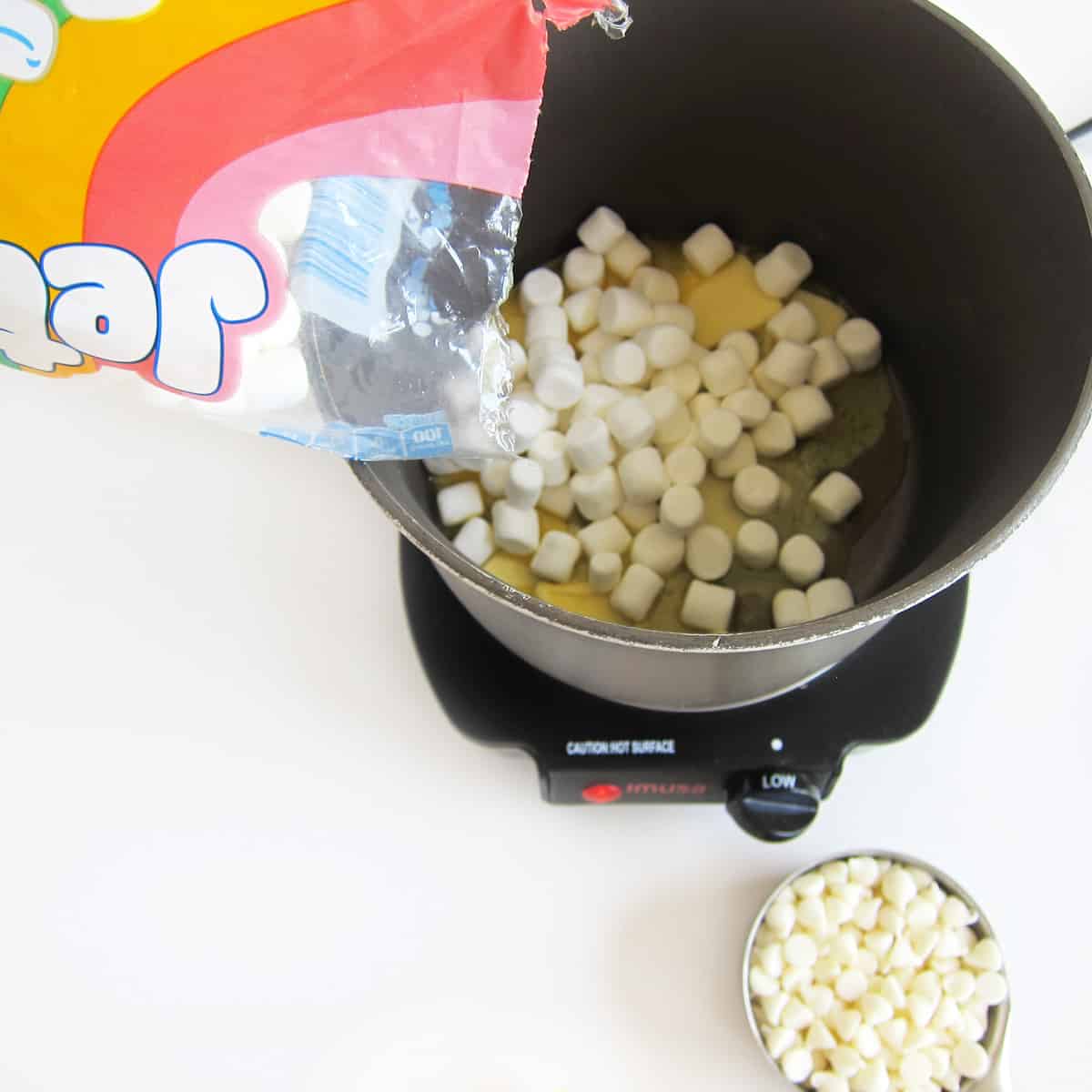 Pouring mini marshmallows into a saucepan with melting butter.