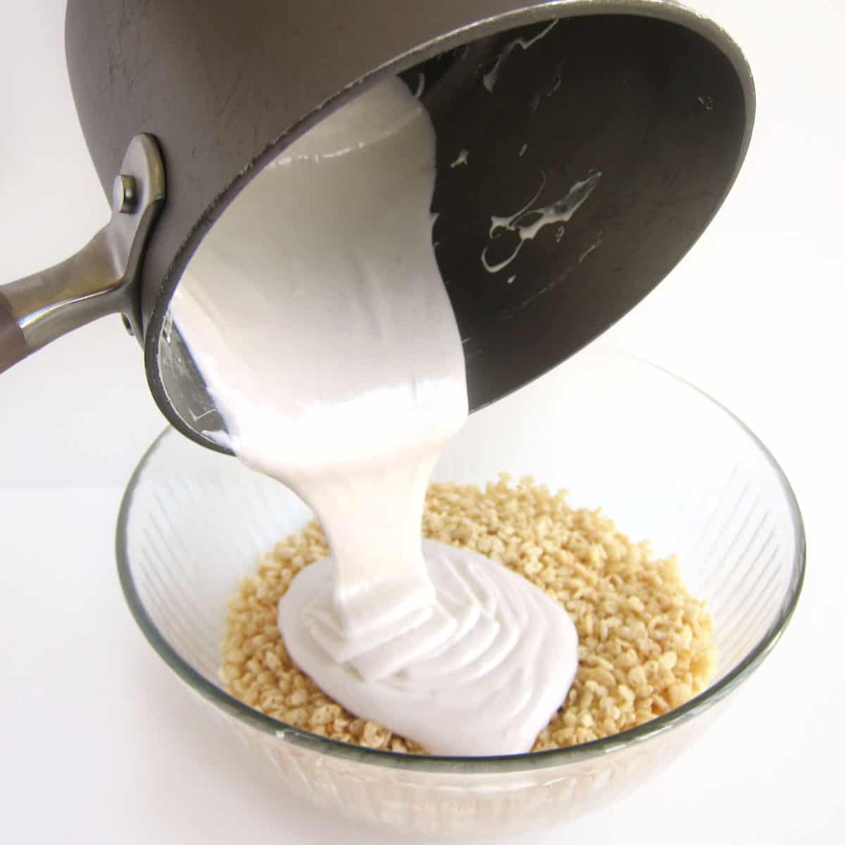 Pouring melted coconut oil and marshmallows over a bowl of crisp rice cereal.