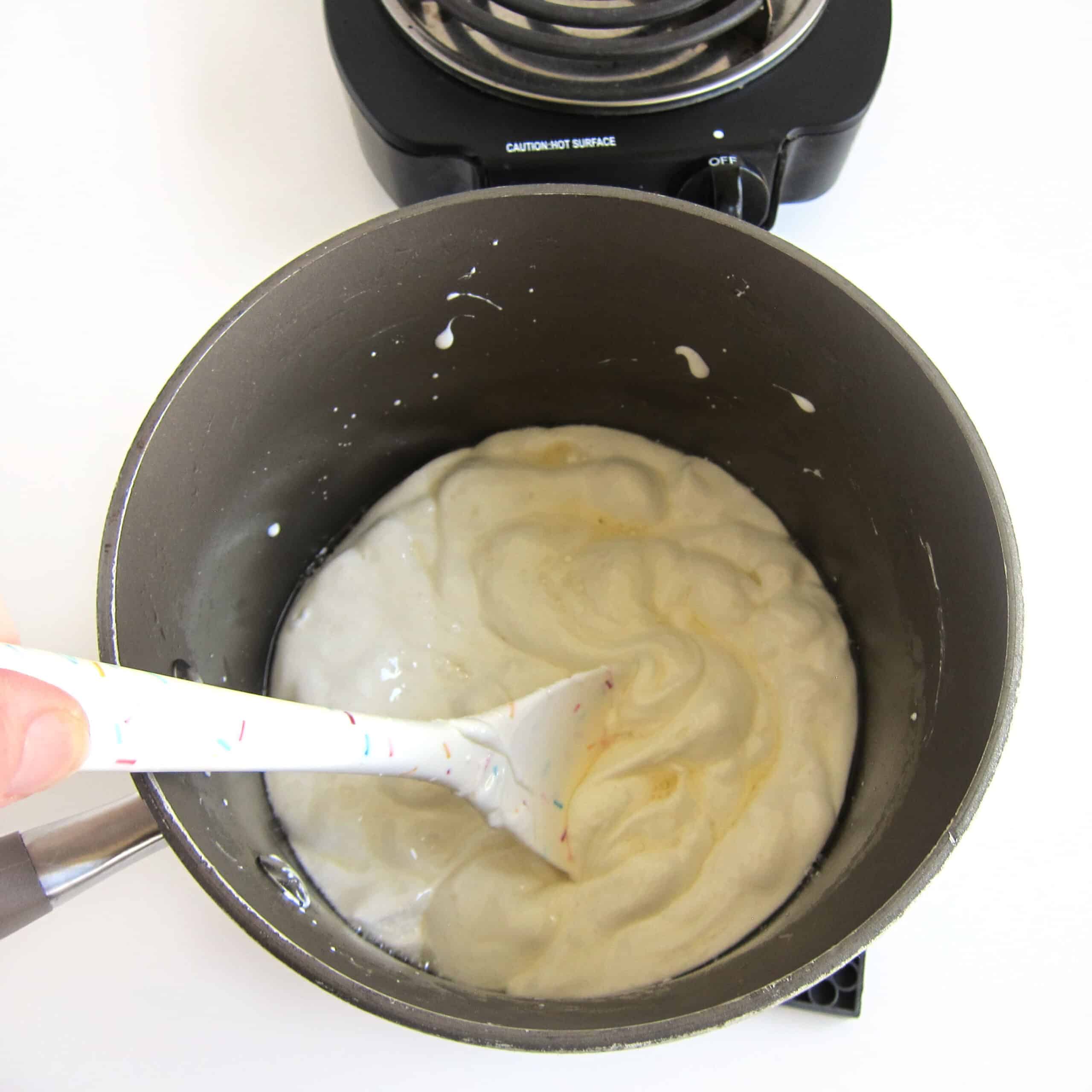 Stirring melted coconut oil and marshmallows in a saucepan using a silicone spatula.