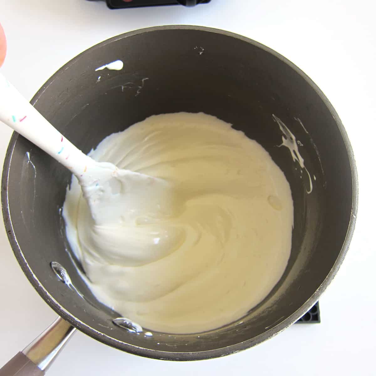 Creamy melted coconut oil and marshmallows stirred with a silicone spatula in a saucepan.
