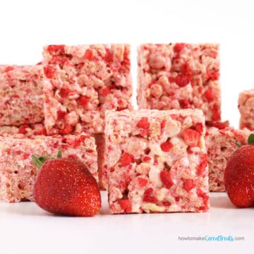 Strawberry Rice Krispie Treats speckled with freeze-dried strawberries are stacked next to fresh strawberries.