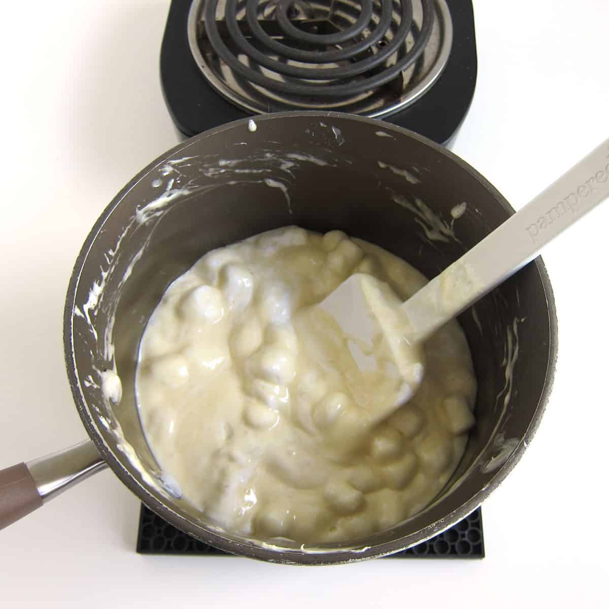 saucepan with partially melted butter, marshmallows, and white chocolate off the stove on a silicone mat.