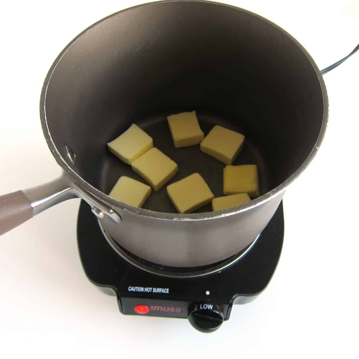 slices of butter in a saucepan set on a small stovetop.