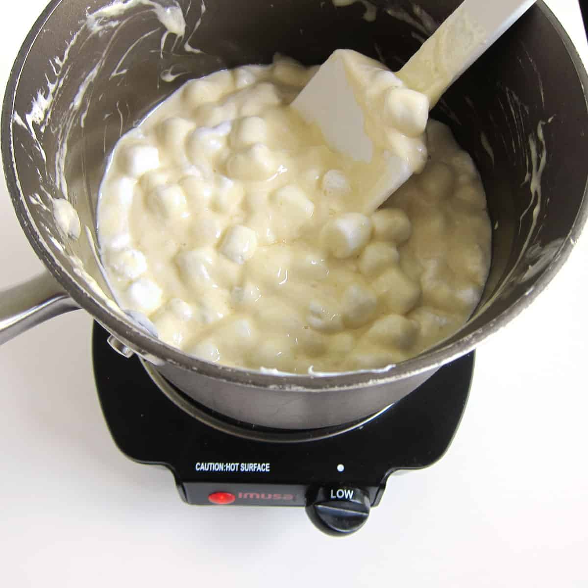 butter, white candy melts, and mini marshmallows melting in a saucepan set over low heat.