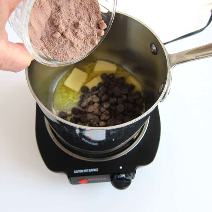 pouring hot cocoa mix with mini marshmallows into a pan filled with melting butter and chocolate chips.