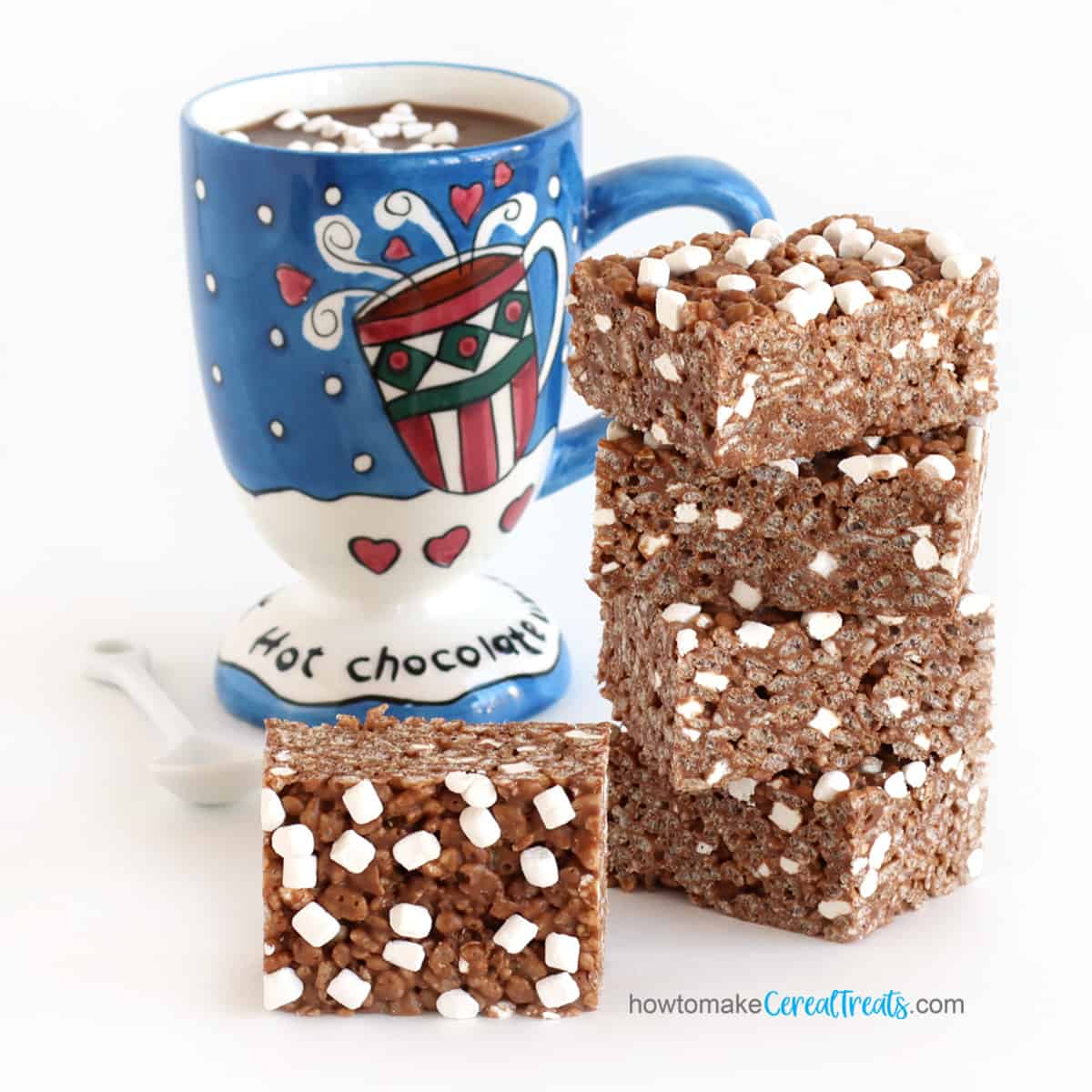 hot chocolate Rice Krispie treats stacked next to a mug of hot cocoa topped with tiny marshmallows.