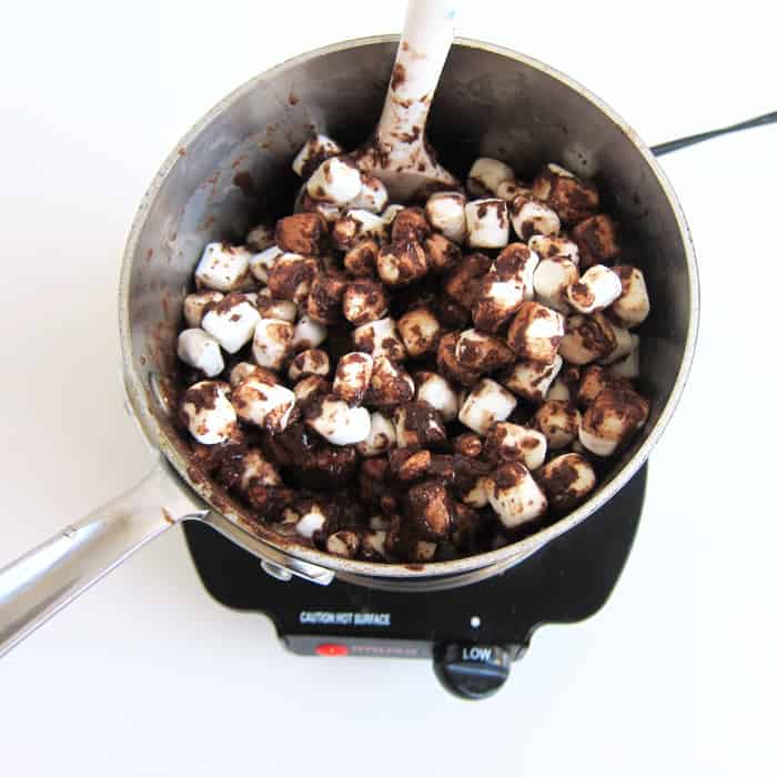 Stirring mini marshmallows into the melted butter, chocolate, and hot chocolate mixture.