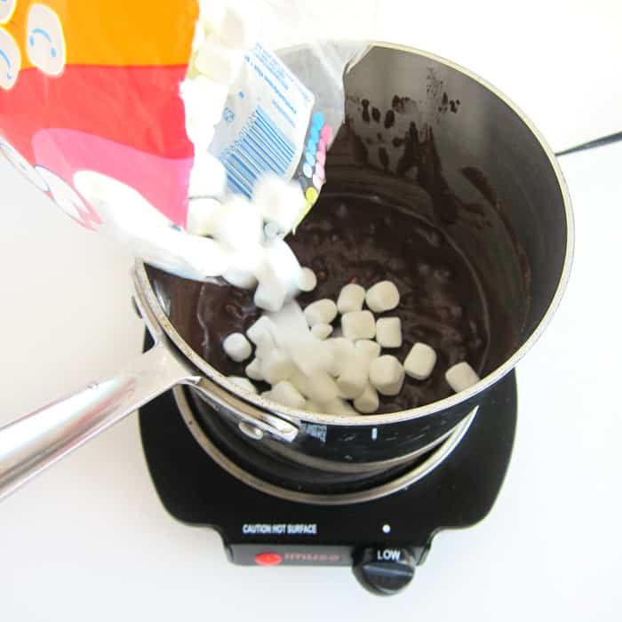 pouring mini marshmallows into the pan with melted butter, chocolate chips, and hot cocoa mix.