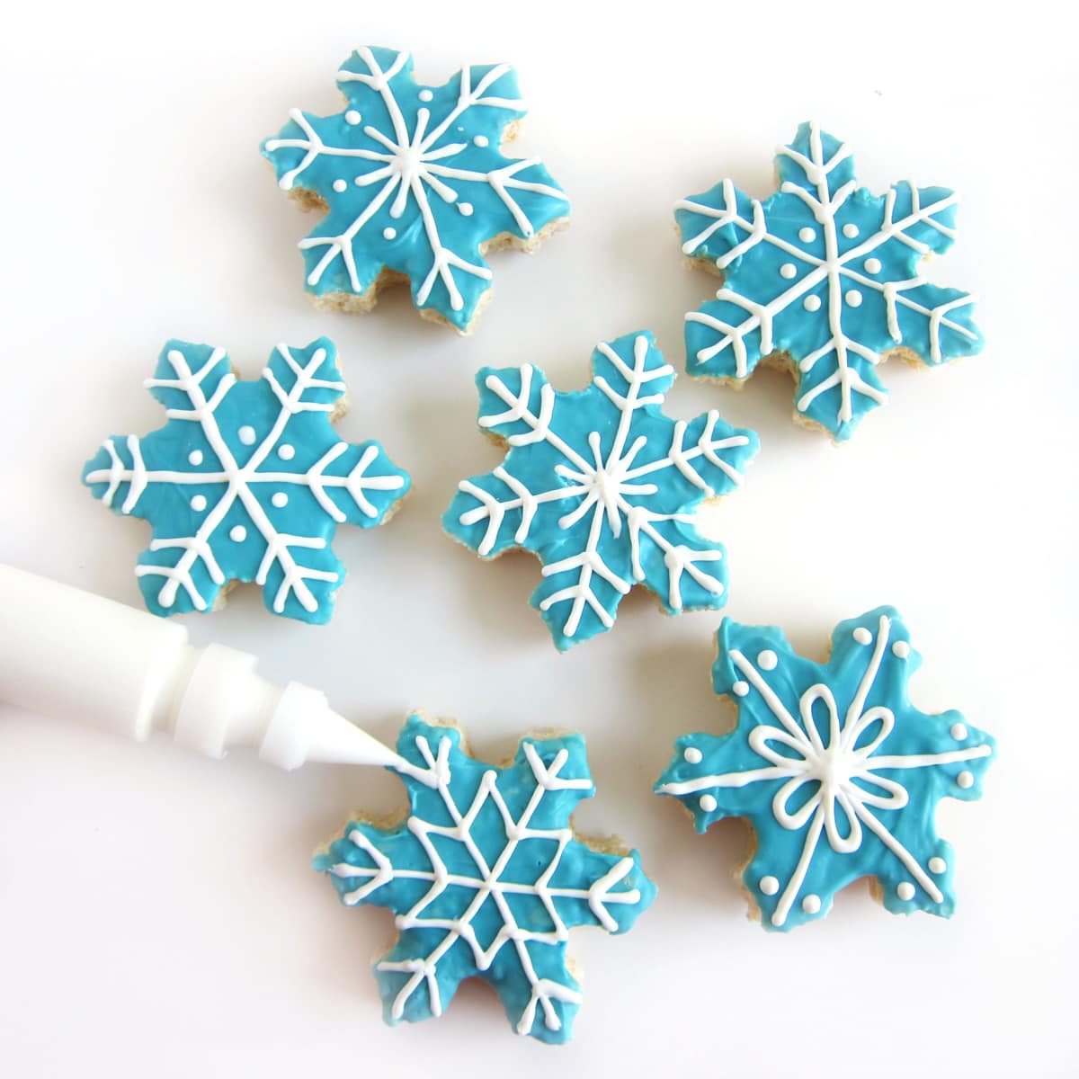six blue-colored Rice Krispie Treat snowflakes decorated with a variety of white chocolate snowflake designs.
