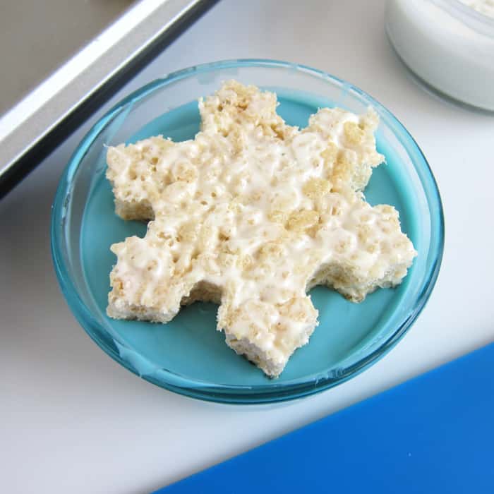 dipping a rice krispie treat snowflake into a bowl of melted blue candy melts.