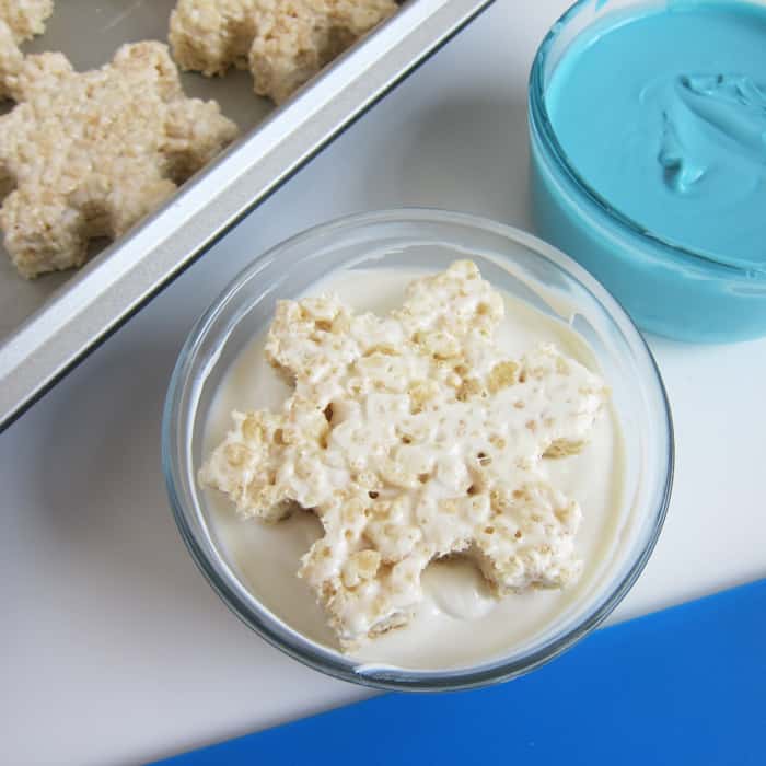 dipping a snowflake rice krispie treat into a bowl of melted white chocolate.