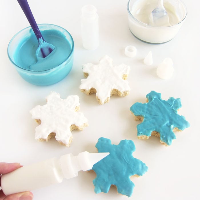 blue and white chocolate dipped Rice Krispie Treat snowflakes with bowls of melted blue and white chocolate.