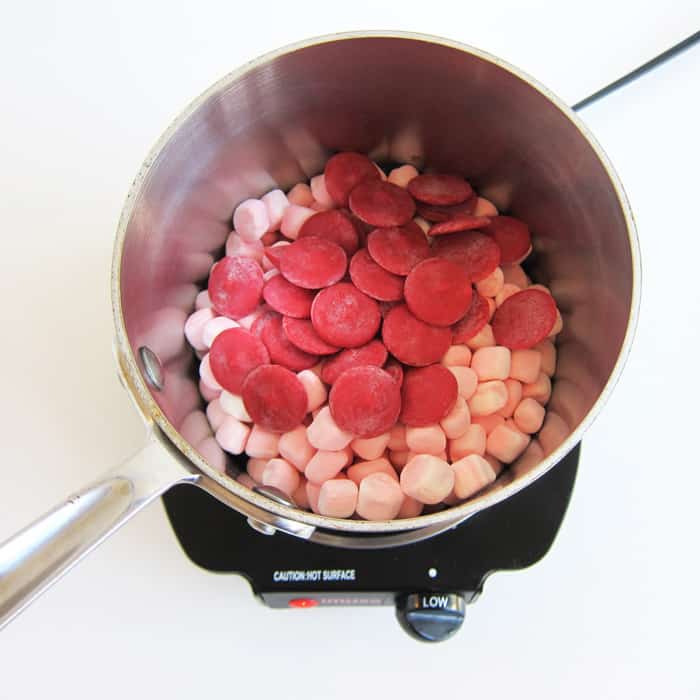 peppermint marshmallows and red candy melts on top of melted butter in a saucepan.