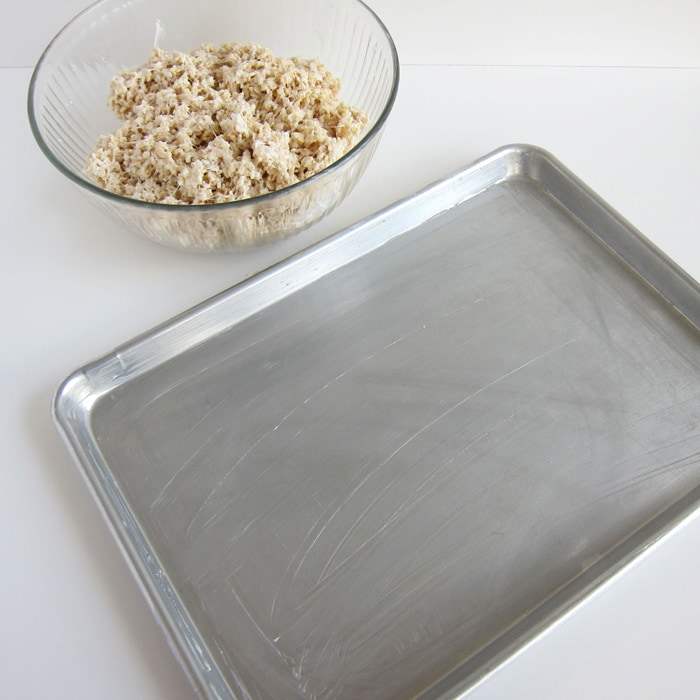 mixing bowl of Rice Krispies Treat mixture next to a greased baking tray.