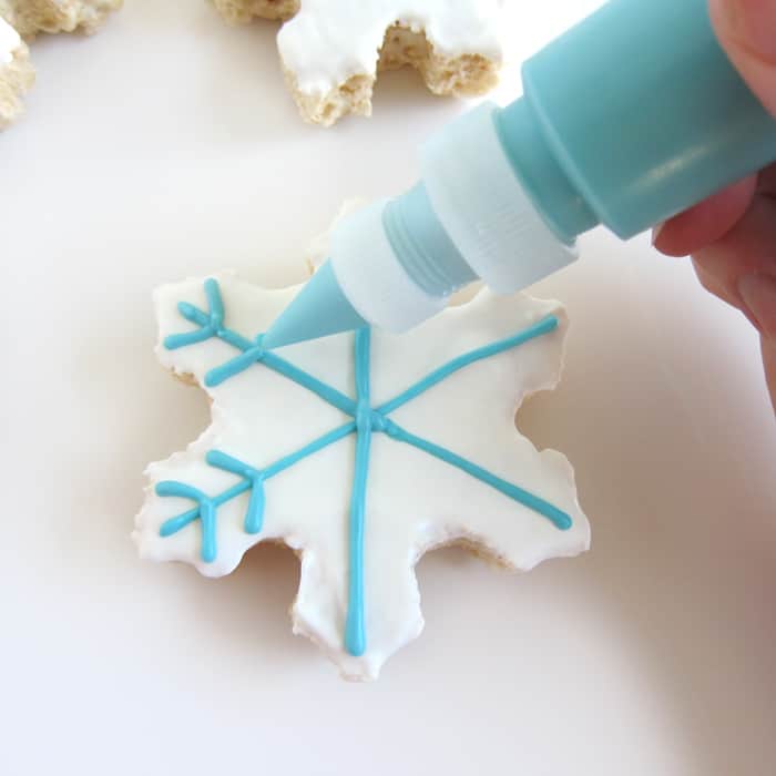 piping blue snowflakes onto white chocolate topped snowflake rice crispy treat.