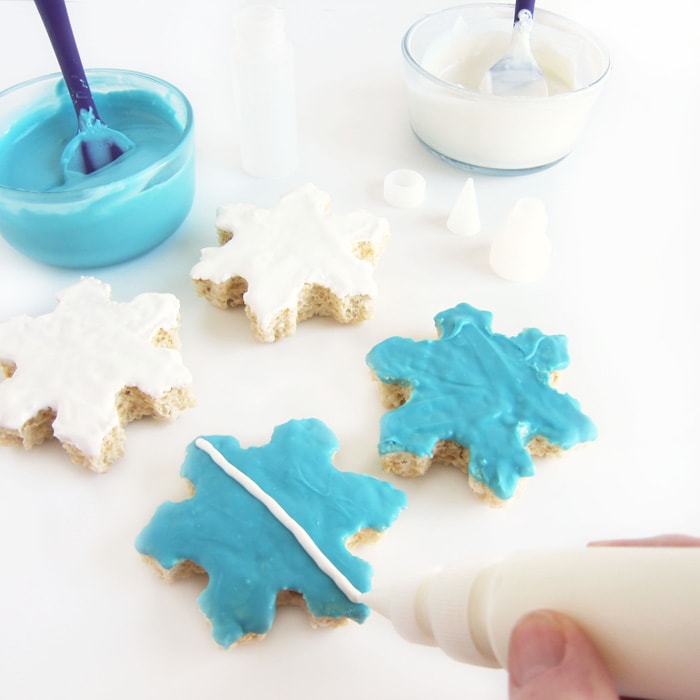 piping a white chocolate line onto a blue snowflake cereal treat.