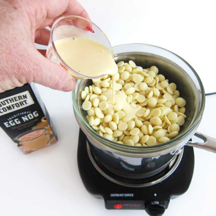 pouring eggnog over white chocolate in the top bowl of a double boiler.