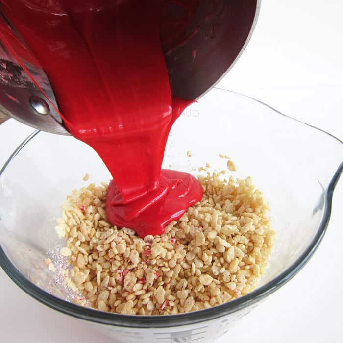 pouring melted red-colored marshmallows over a mixing bowl filled with Rice Krispies Cereal. 