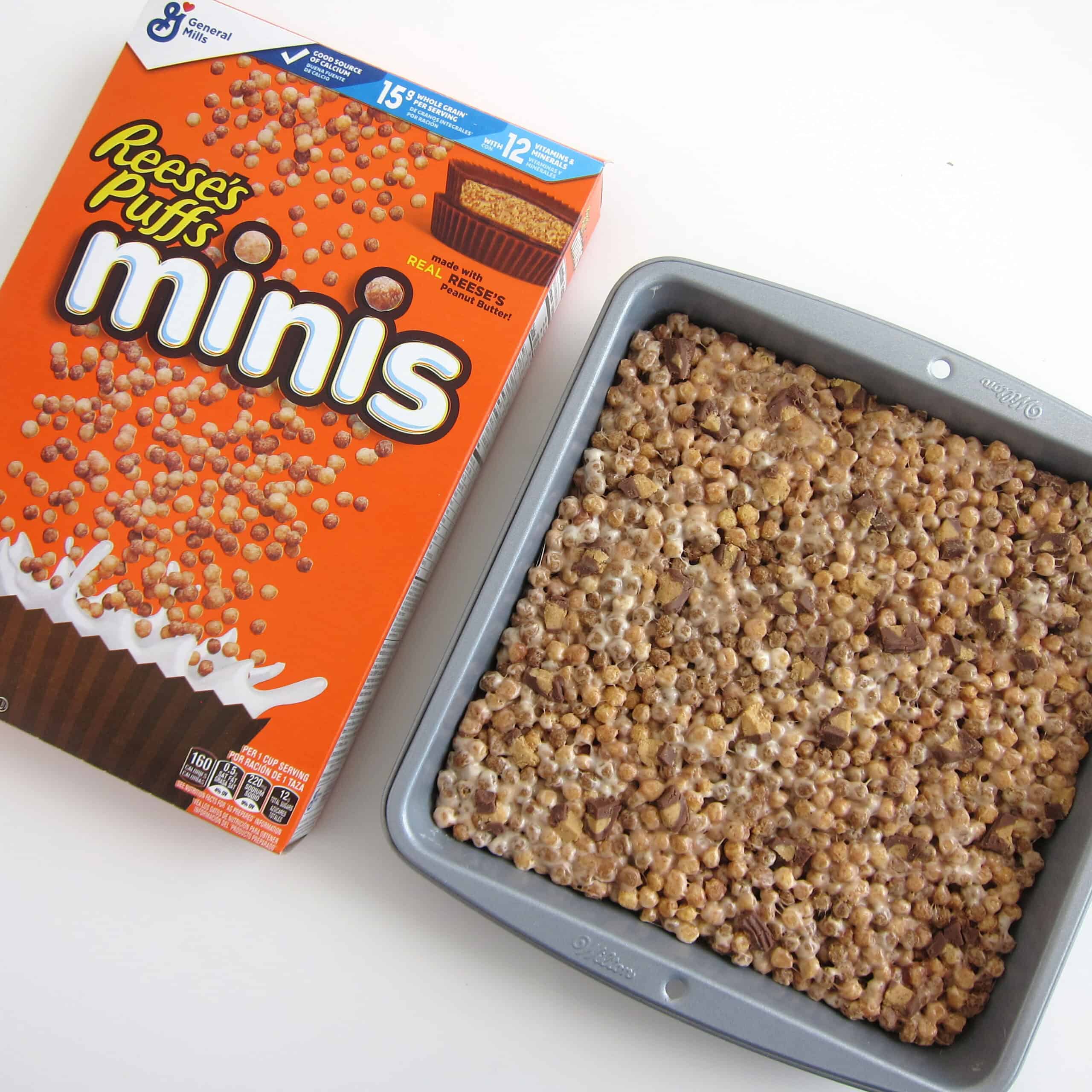 Reese's Puffs Minis Cereal Treats in a baking pan set next to a box of Reese's Puffs Minis cereal.